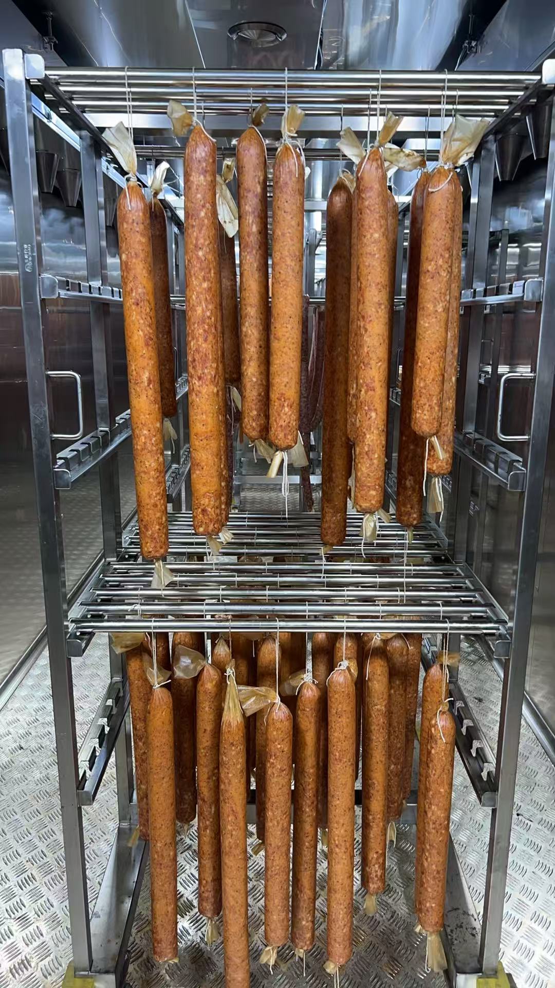 Sausages suspended on stainless steel racks inside a modular cold-smoking chamber